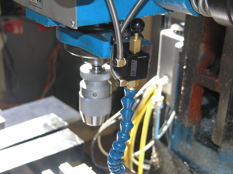 Blue drill press with black device and spiral metal rod.