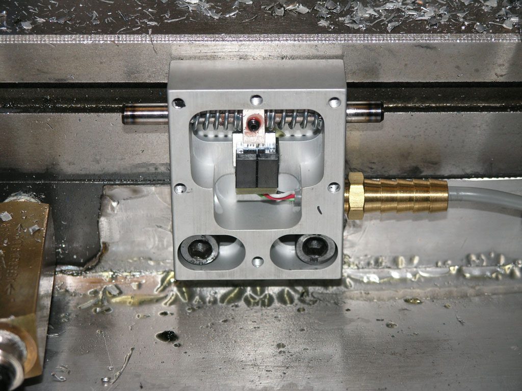 Metal component with square cutout and drilled holes on a metal surface.