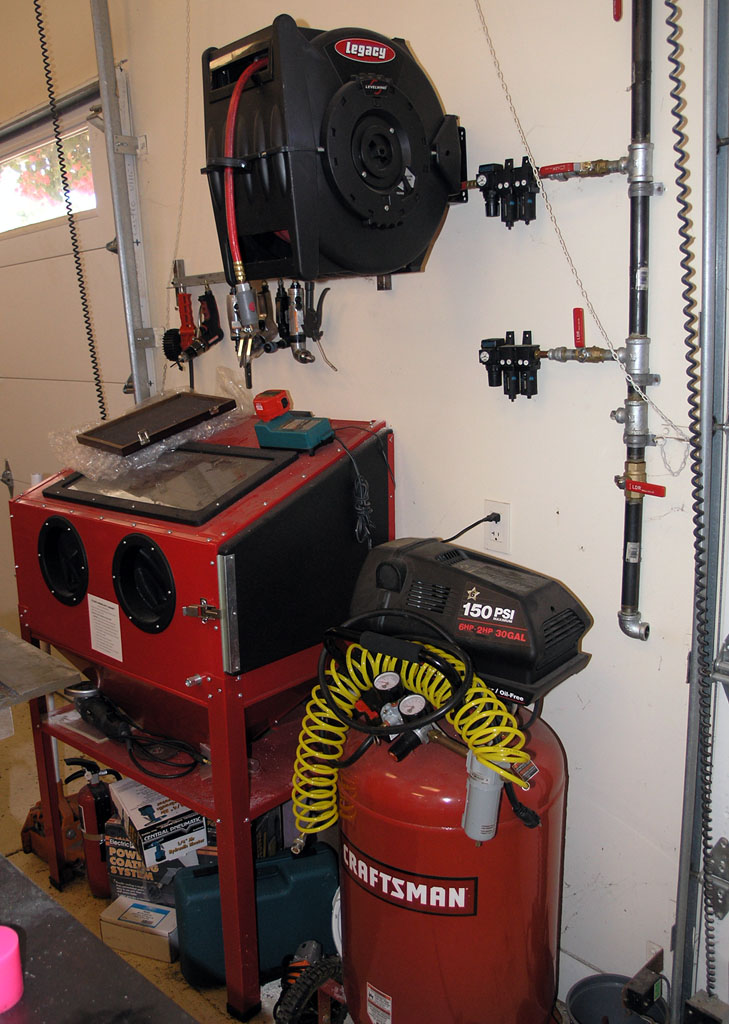 Well-organized garage with air compressor, sandblaster, and air hose reel.