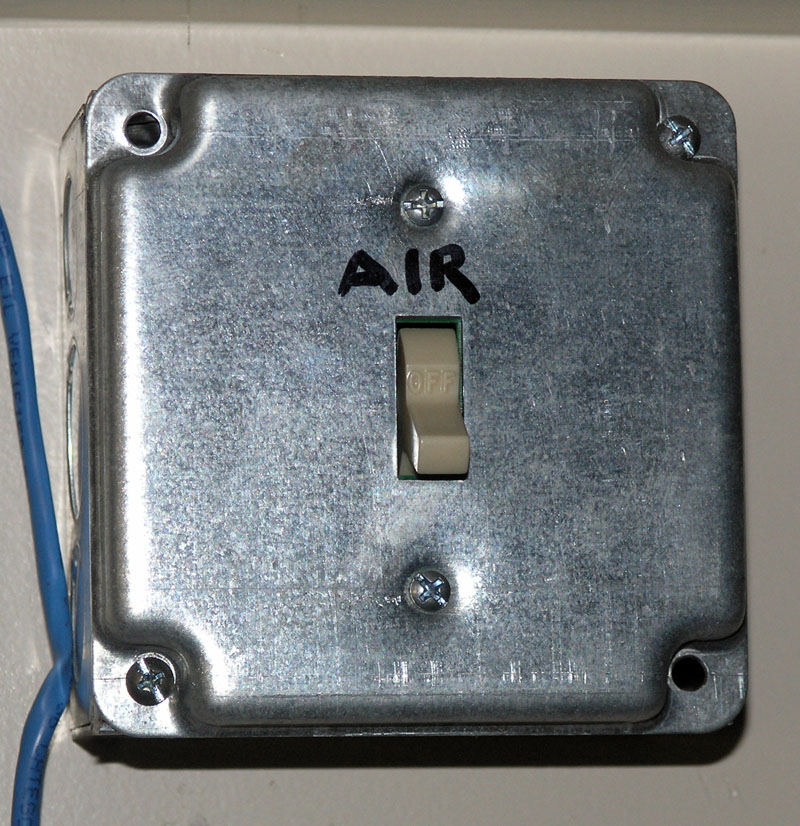 Metal electrical box with air switch mounted on wall, blue cable attached.