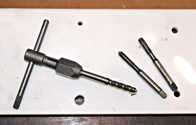 Metal tools with threaded ends on a white surface.