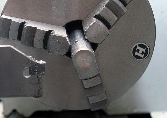 Metal tool with round knob and three rectangular protrusions on a gray background.