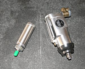 Silver metal cylinder with green tip and silver metal disc on gray background.