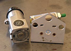 Silver cylindrical metal component with black label beside white metal bracket on gray concrete floor.