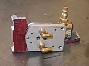 Machine parts including red block, metal plate, and brass fitting, likely for machining or metal fabrication instruction.