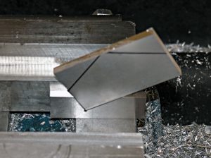 Metal being cut or shaped by a machine tool, with metal fragments and shavings surrounding a sharp-edged piece.