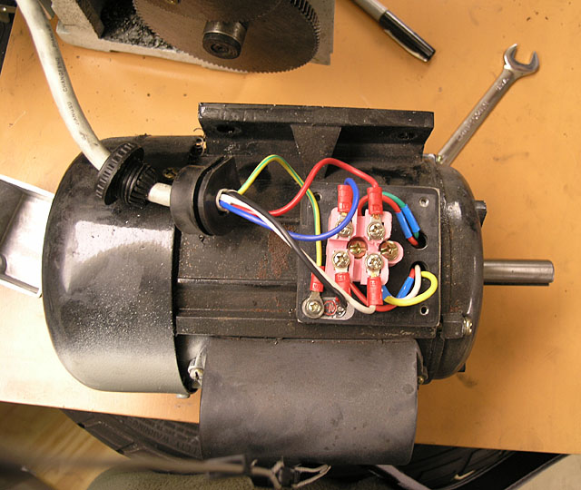 An electric motor with exposed wiring on a workbench among various tools.