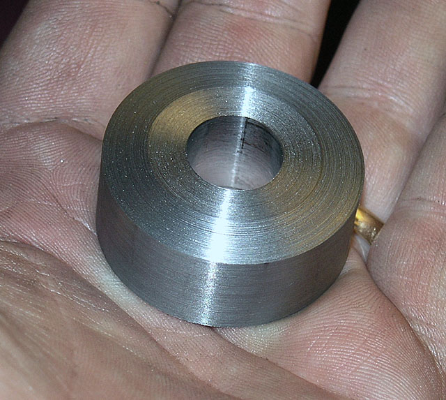 A cylindrical metal object with a circular hole and brushed finish resting on a hand.