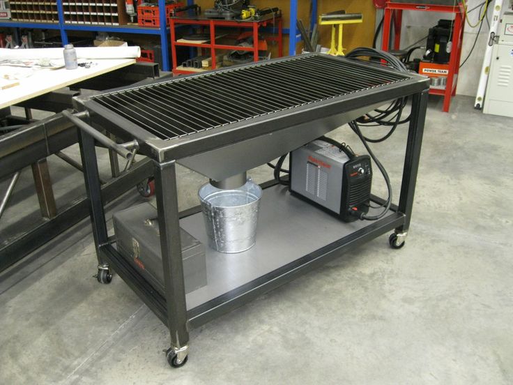 Plasma cutting table with metal grate, integrated welding machine, and casters in a workshop or garage setting.