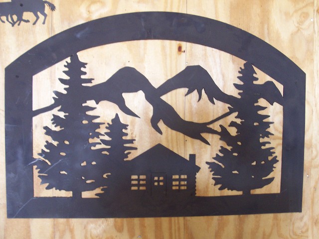 Black metal sign with mountain, tree, and house design on a wooden background.