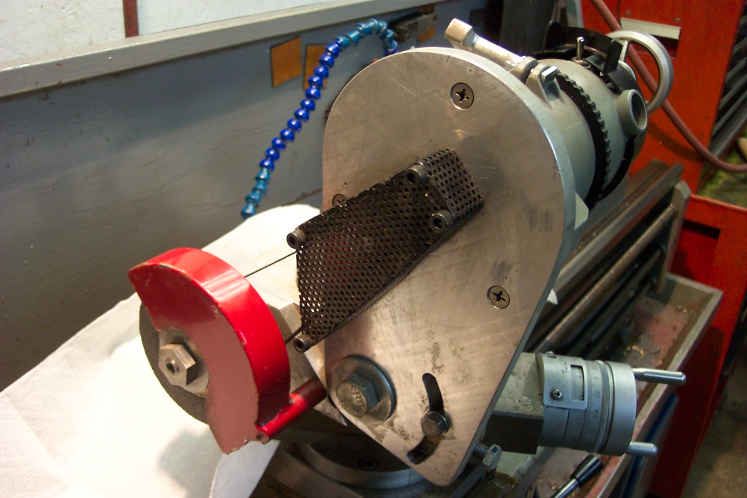 Industrial grinder with red wheel and metal plate on a background of machinery and tools in a clean workshop environment.