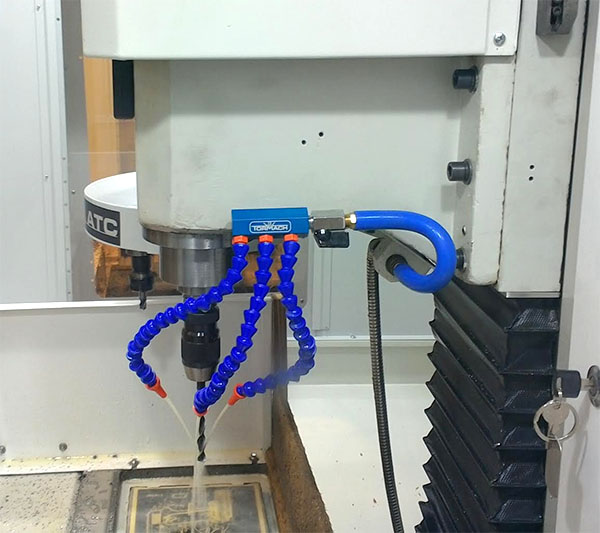 Flexible coolant delivery system attached to a large white machine with three curved nozzles.
