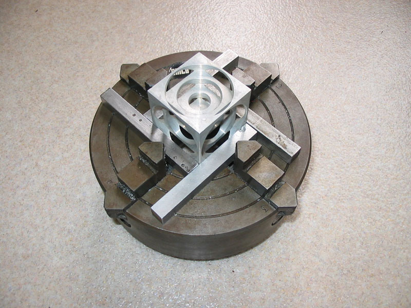 Precision tooling component with central cube surrounded by concentric grooves in an angular metal frame.