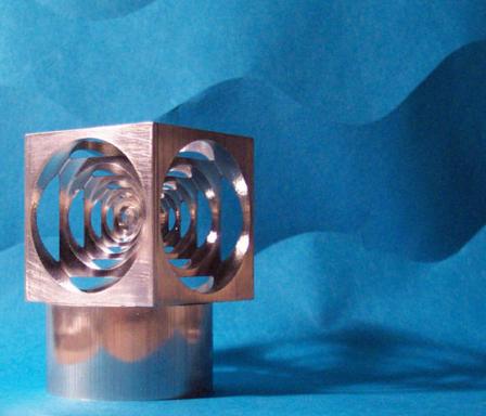 Silver metal cube with circular cutouts and cylindrical base on a blue background.