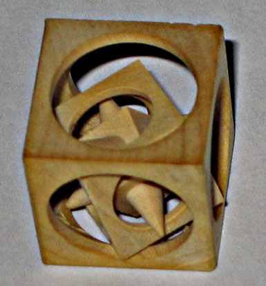 A 3D wooden cube with circular cutouts and a star-shaped hole.