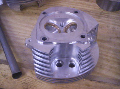 Metal component with two circular holes and ribbed edge on wooden surface. Made of aluminum.