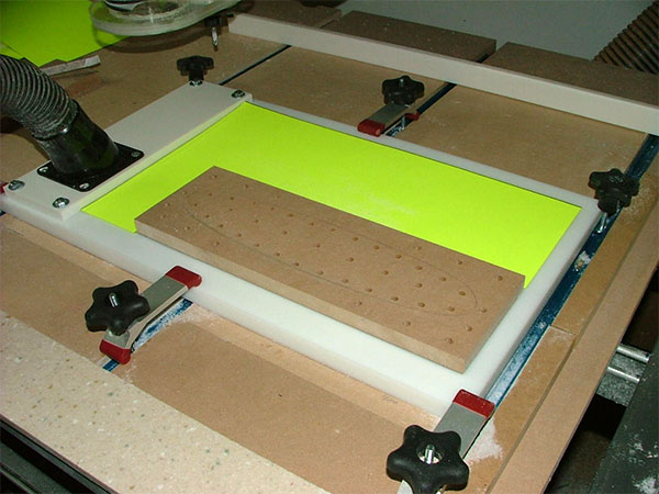 Vacuum table with yellow insert and black hose, used in machining processes.