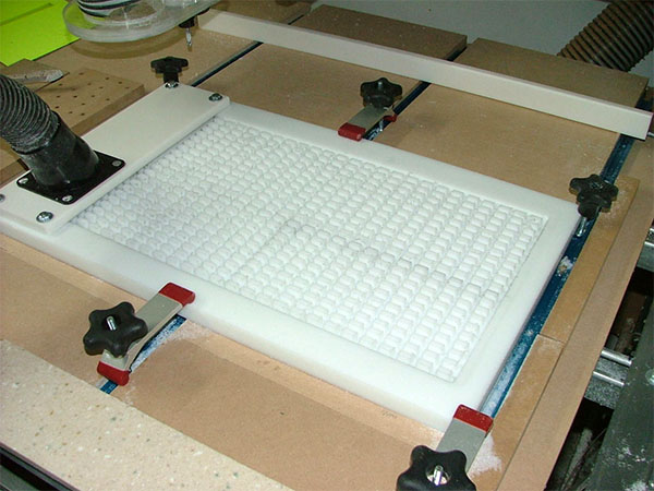 A vacuum table with a white surface and red/black knobs attached to a wooden frame.