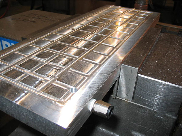 A rectangular metal plate with a grid pattern and a cylindrical protrusion.