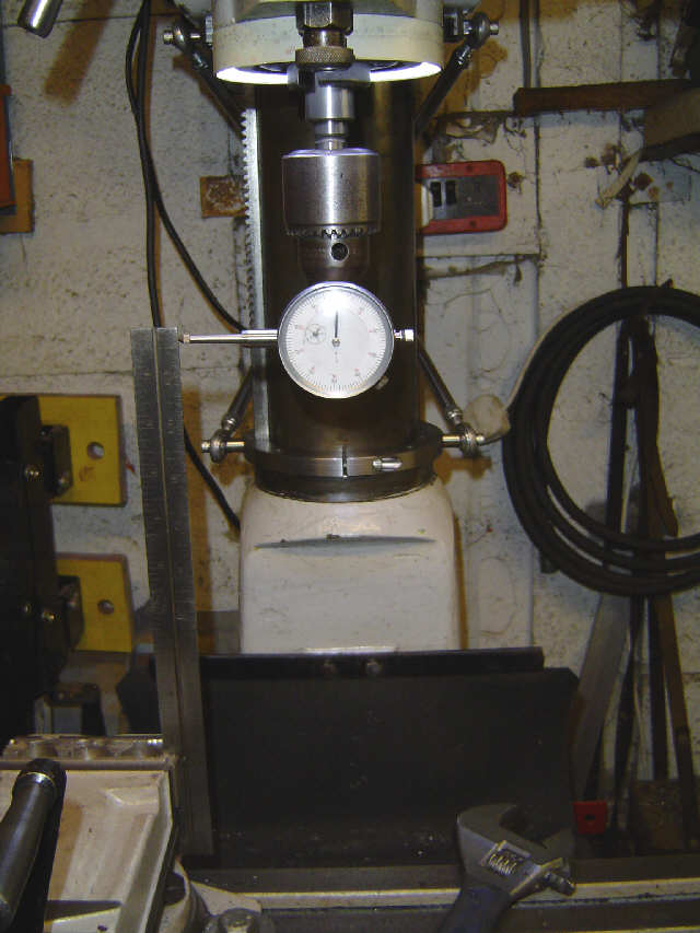 Metal machine with round white dial in workshop setting, surrounded by tools and equipment.