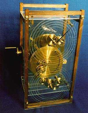Antique brass mechanical device with glass front and wooden case, featuring dials and pointers.