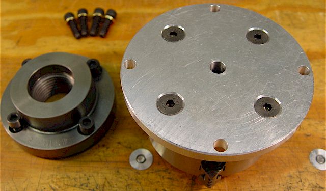Metal components including 4-jaw chuck adapter plate on wooden surface.