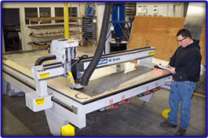 Man standing beside white machinery with glass table in workshop setting.