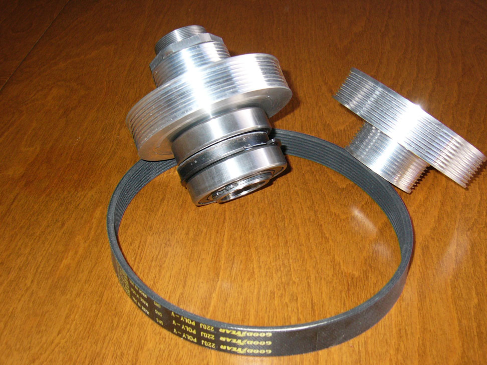 Mechanical components, including a belt and pulleys, on a dark wood grain background.