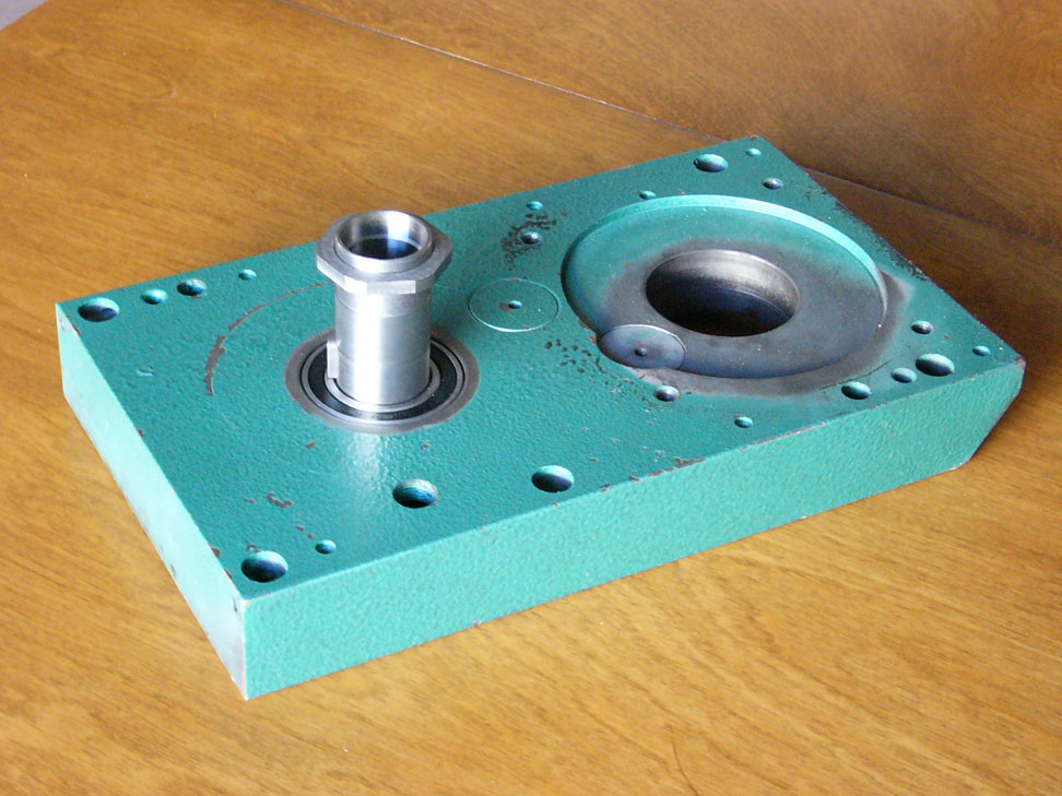A green metal part with two circular holes, sitting on a wooden table.