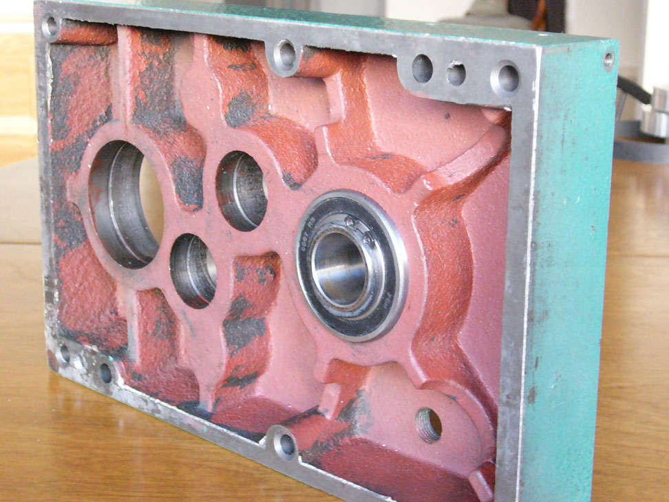 Industrial component with red plastic casing and four circular openings on a wooden table.