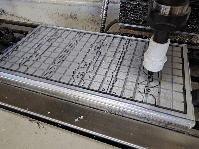 Metal CNC machine table with grid patterned surface and metal construction featuring small holes and an out-of-focus industrial background.