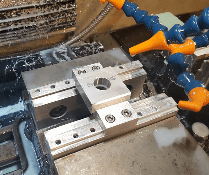 Metalwork setup in workshop with silver metal piece and blue orange clamps.