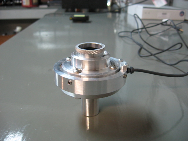 Silver cylindrical metal component with threaded opening sitting on gray surface.