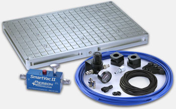 Vacuum chuck system with blue base and various components, featuring a small metal object and a gray rectangular object with grid pattern.