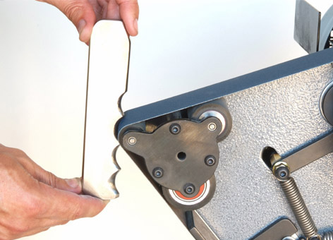 A person's hand holds a white object with a serrated edge next to a metal surface.