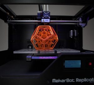 A MakerBot 3D printer with an orange object being printed on its platform.
