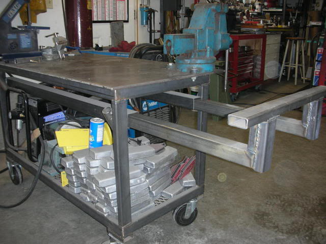 A sturdy welding table with a flat surface and metal frame, featuring casters and organized tools.