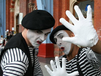 Two people dressed as mimes posing in front of a brick building.