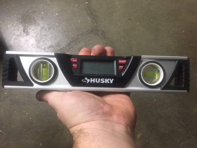 A person's hand holding a HUSKY digital level with three circular displays showing green lines.