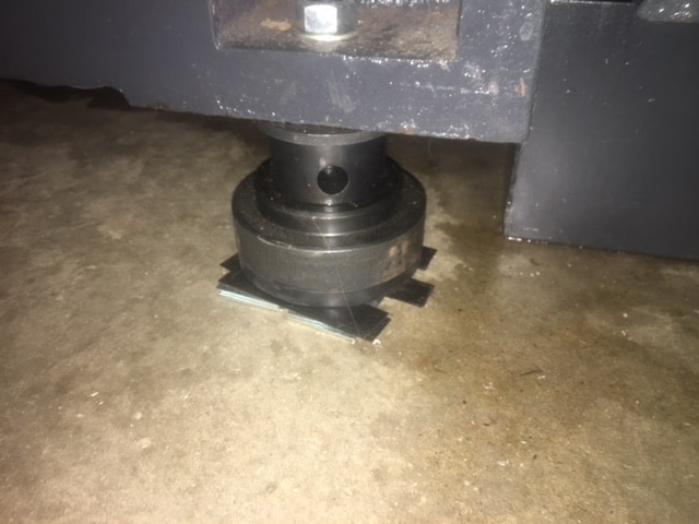 A black metal shim attached to a black metal object on a concrete floor using screws.