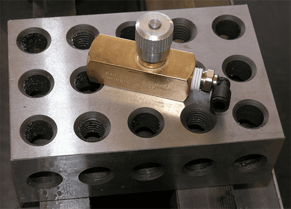 Metal tool with brass component and multiple circular holes on a dark background.