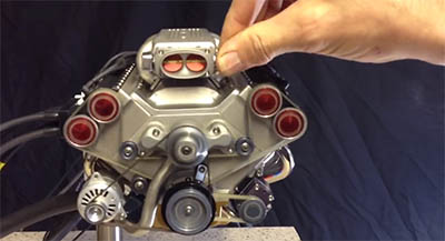 Quarter-scale V8 model engine's rear section with red circular components and black cylindrical component on dark background.