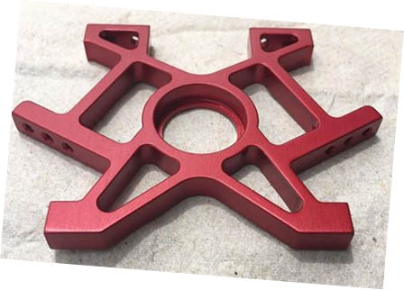 Red alloy part with central hole and X-shaped design.