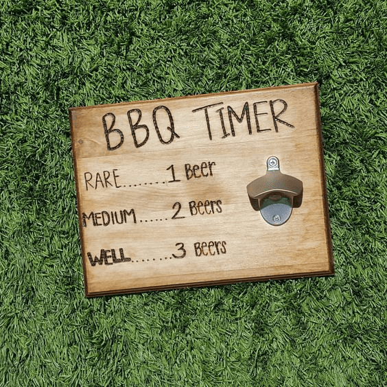 A wooden sign with a BBQ timer display on a grassy surface featuring a list of beer quantities and corresponding cooking times.