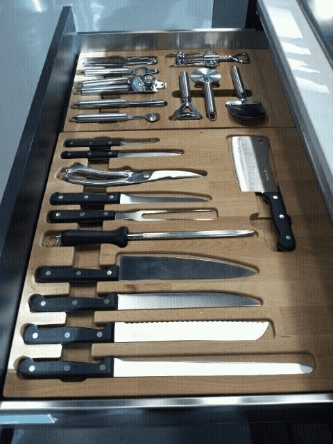 Kitchen utensils and knives arranged in wooden drawer organizer.