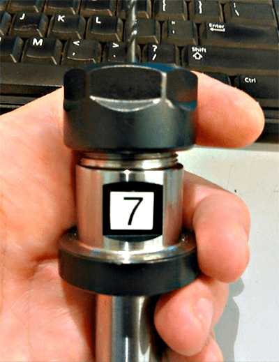 A close-up photo of a calibration tool with a black top and silver base featuring the number "7".