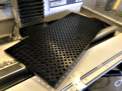 Black rubber mat with holes on top of a metal surface in a workshop or machine shop setting.