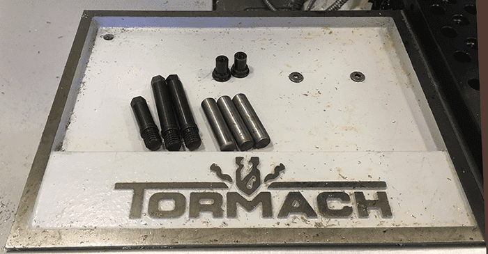 Tormach brand metalworking tool on a metal work surface with various tools and parts in the background.