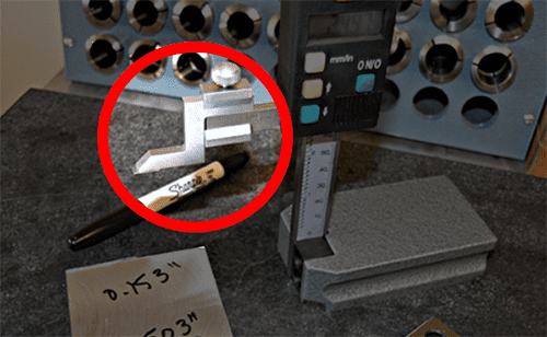 Metal cutting tool with angled blade on grey surface amidst machining tools and machinery.