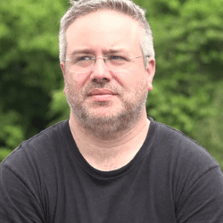 Man with gray hair and glasses wearing a dark shirt.